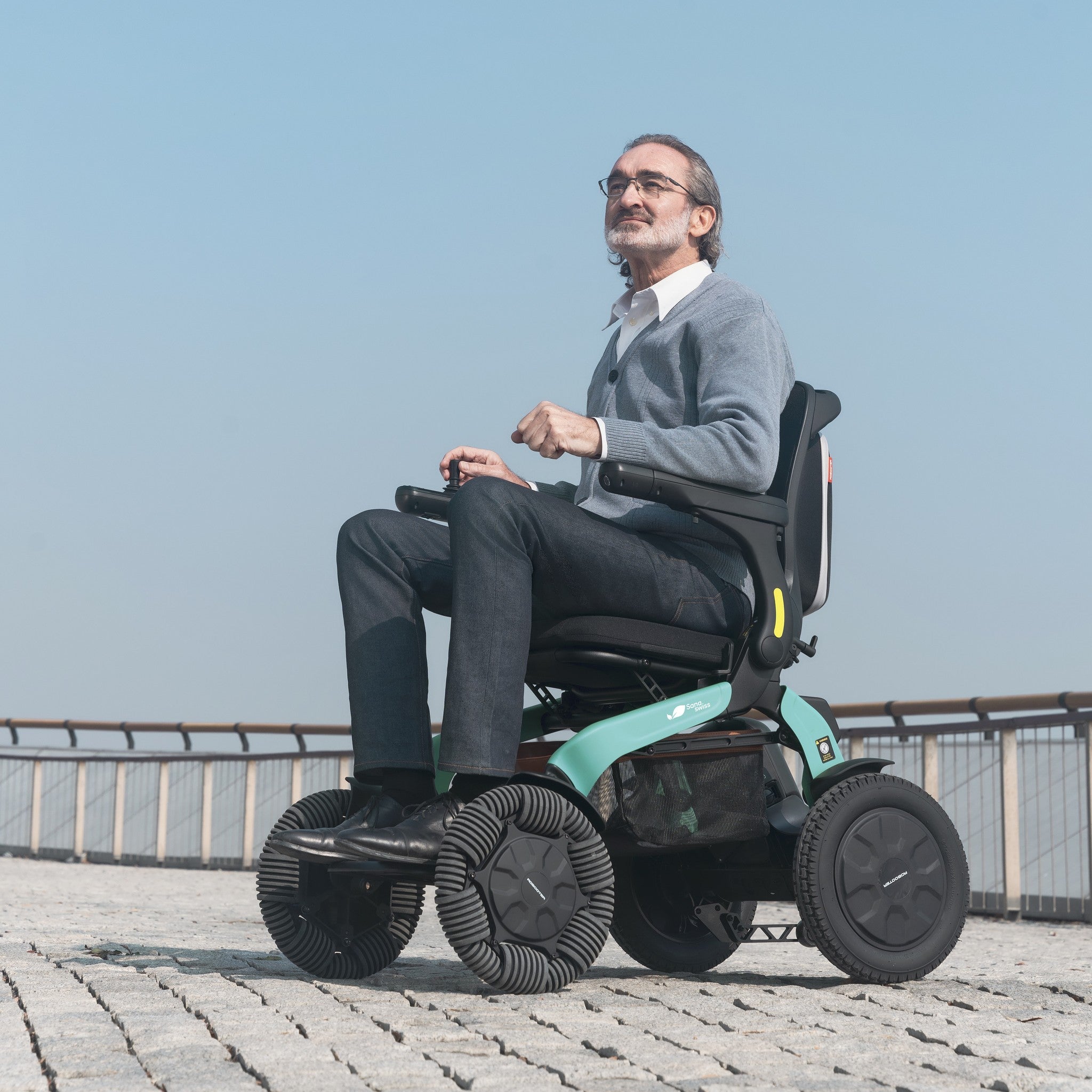 Mann fährt mit dem Elektrorollstuhl E60 Pro Outdoor über Kopfsteinpflaster am Ufer