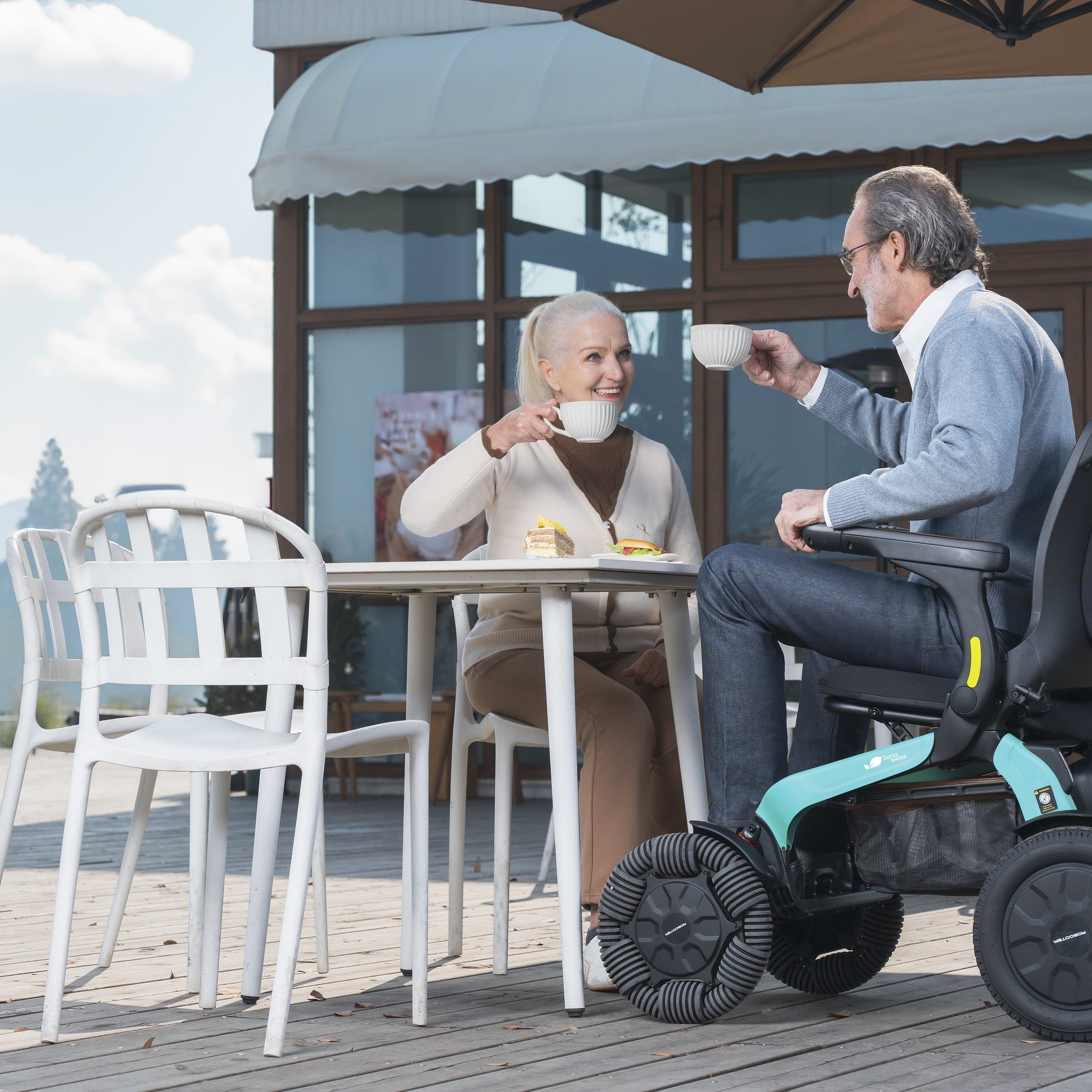 Paar sitzt im Café am Tisch, der Mann bleibt im Elektrorollstuhl E60 Pro Outdoor sitzen
